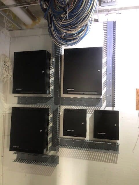 Avigilon access-control and network panels mounted on a backboard with managed cabling